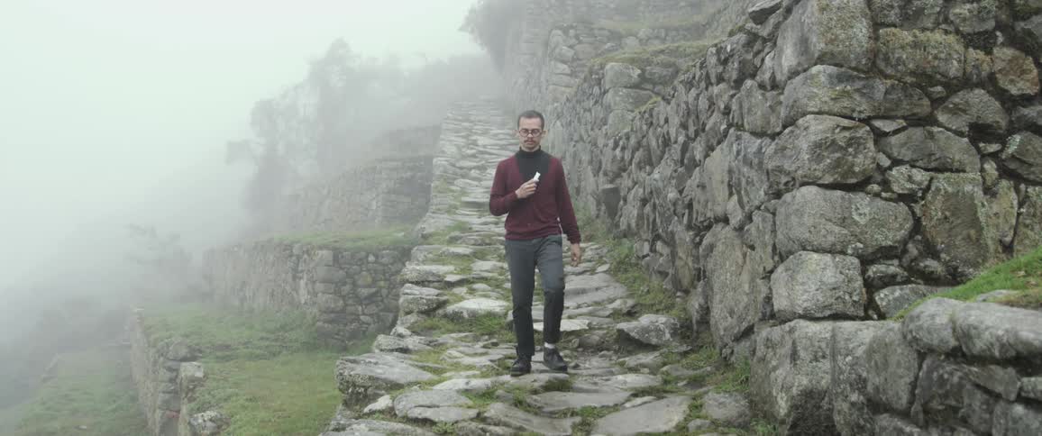 A white man walks down a staircase at an ancient site
