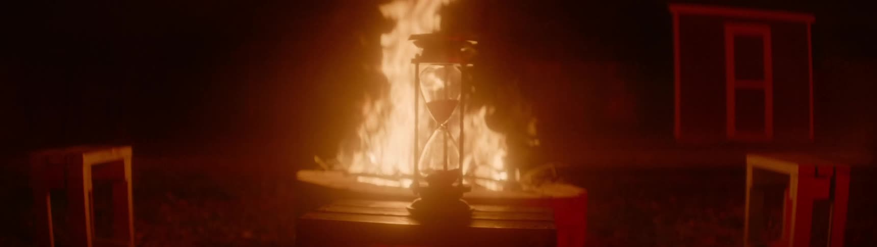 An hourglass sits in front of a fire pit containing a roaring blaze