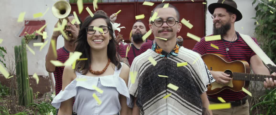 A band follows a couple playing music as confetti falls on the newlyweds