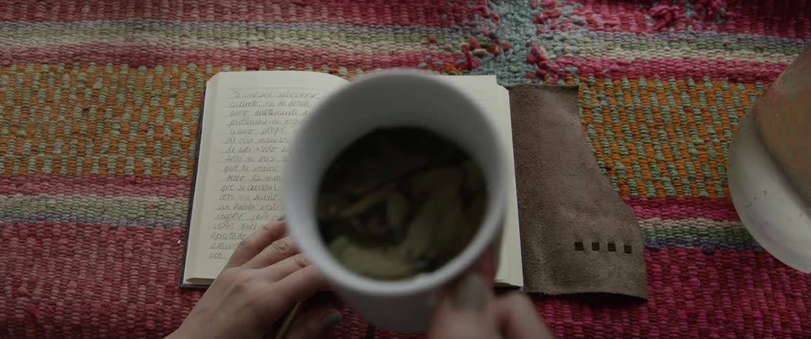 A white woman writing in notebook picks up a coffee cup
