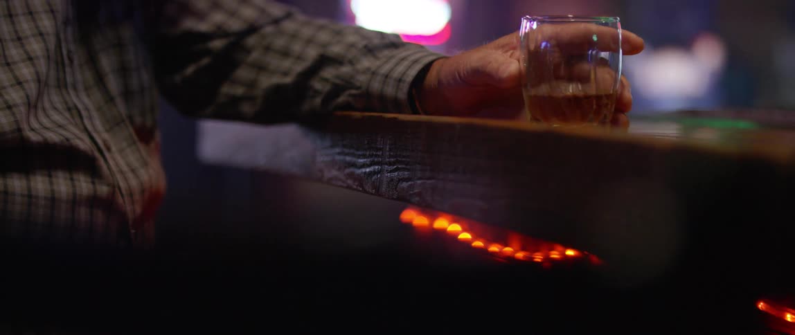 A man at a bar takes a drink and sets his glass on the bar top