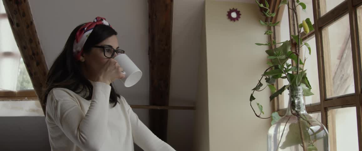 Brunette woman drinks from her cup and looks out the window