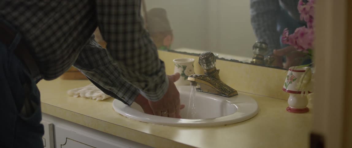 A white man washes his hands in a bathroom sink