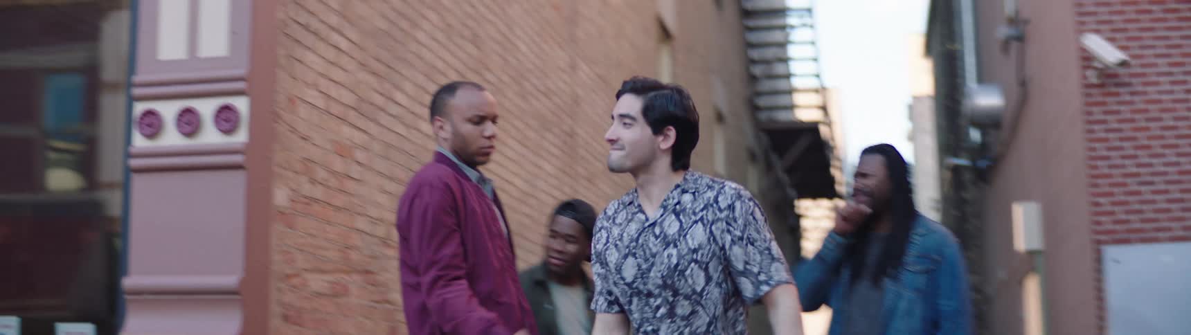 A black man stops a white man from approaching a blonde passerby
