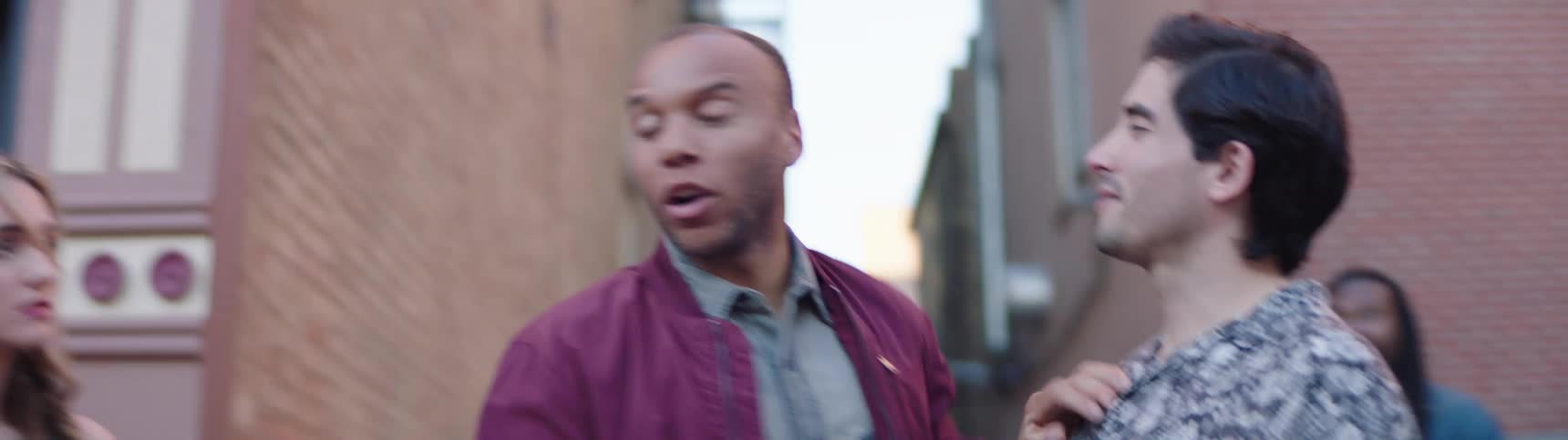 A woman walks by a group of men and one of them grabs her his friend then intervenes and helps the woman