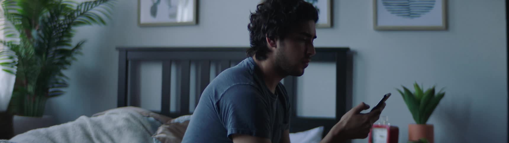 Man sitting on the bed uses his smartphone in the bedroom