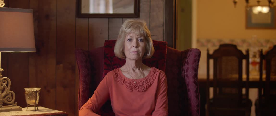 Elderly woman sits in an armchair and stares at the camera