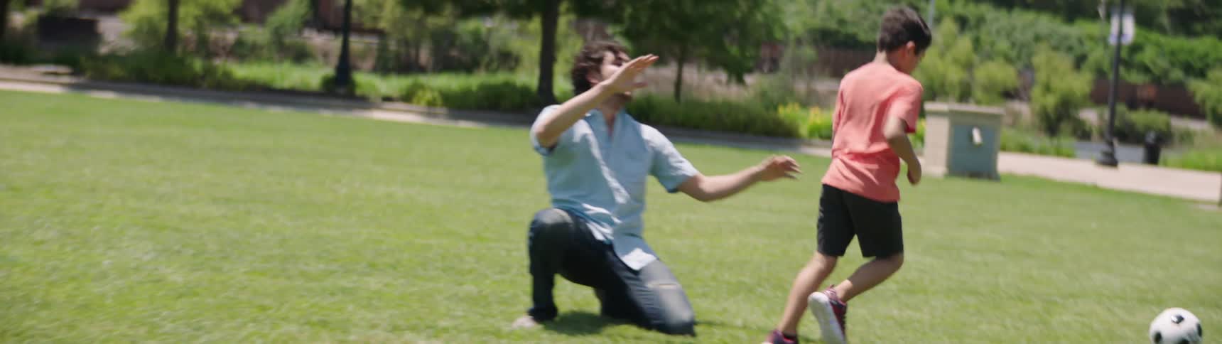 A father laughs as his son steals a soccer ball away from him