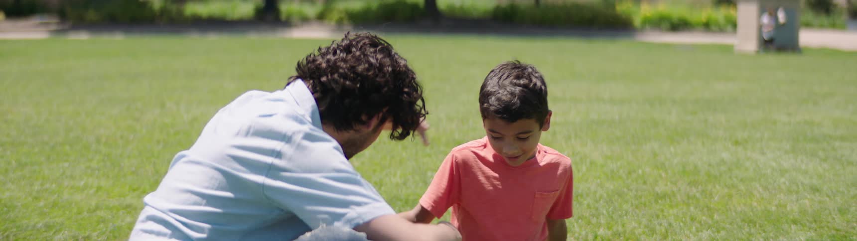 A man rubs his sons hair as they sit on the grass with a soccer ball