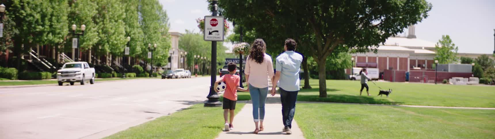 A family walks down a sidewalk in a neighborhood
