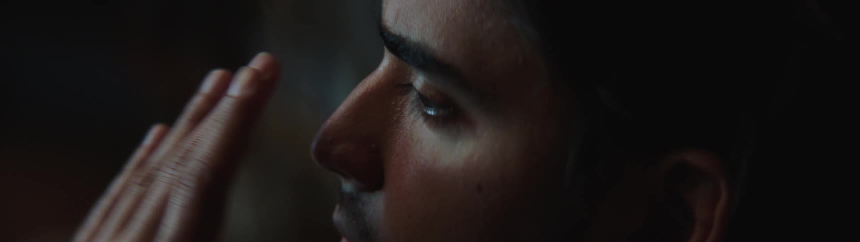 A man rubs his eyes with his hands while watching television