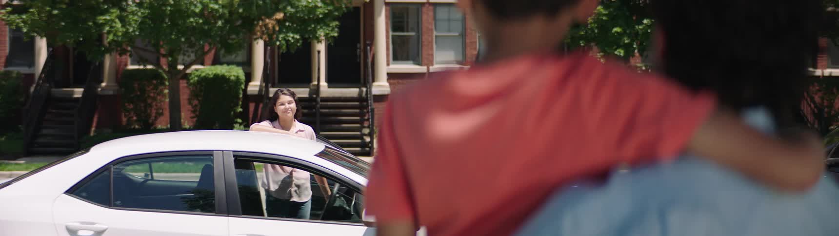 A woman stands at her car and smiles at her husband and son