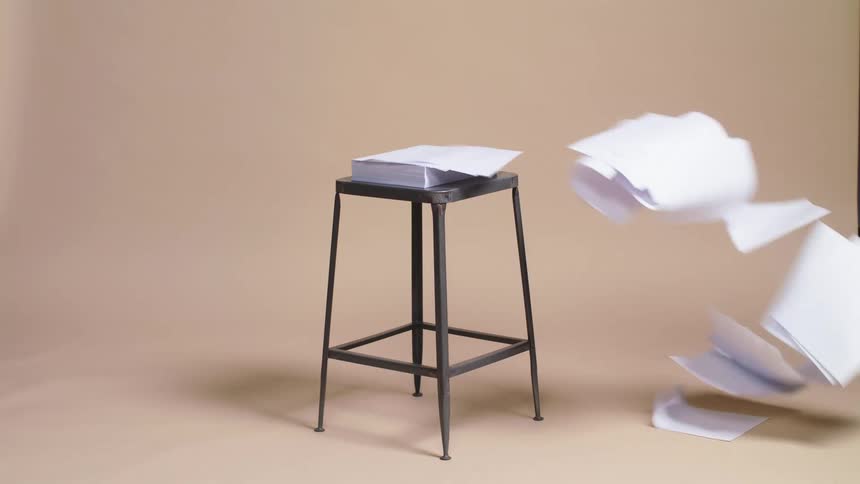 A gust of air blowing sheets of paper from a stack atop a metal stool