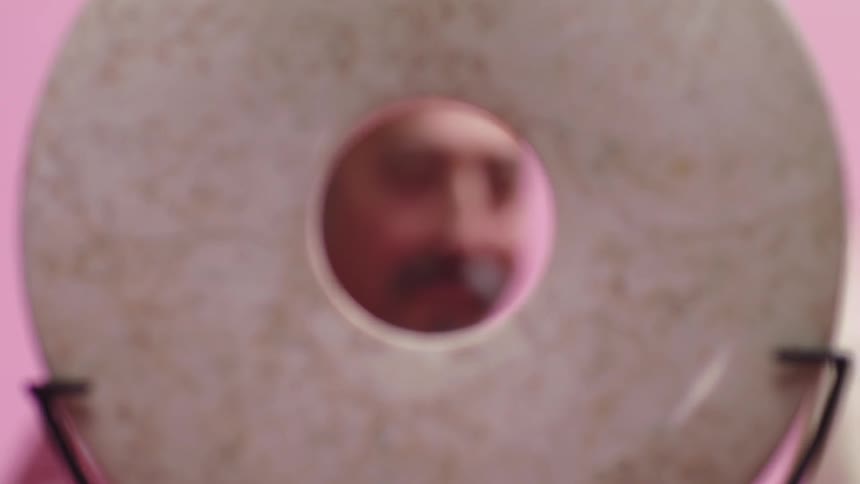 A man stands behind a circular object and is seen in the hole in the middle