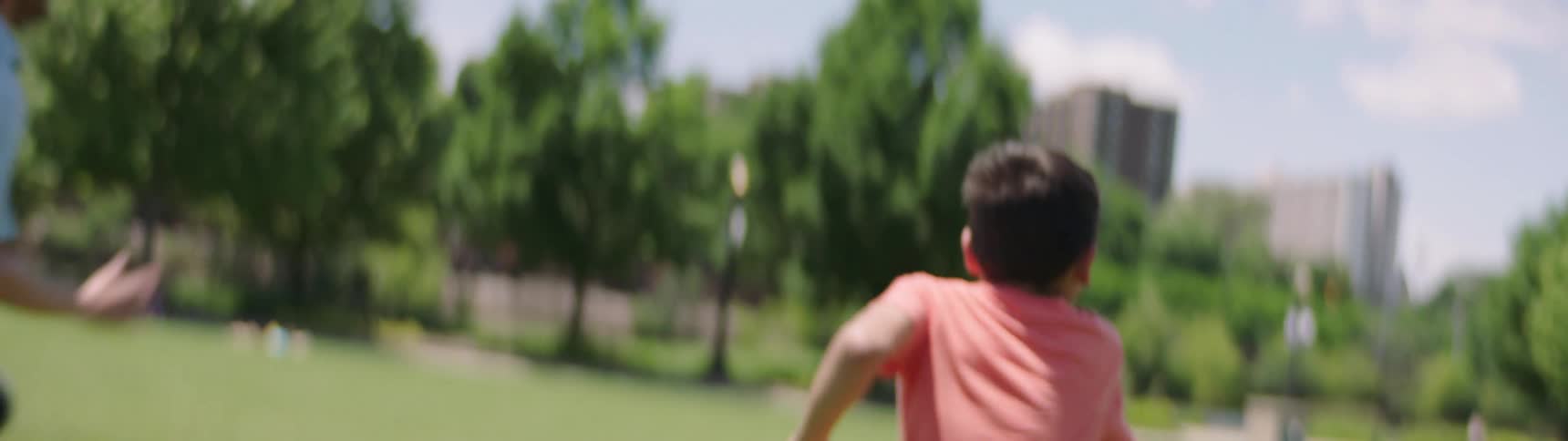 Father and son play football on a green grass in the public park