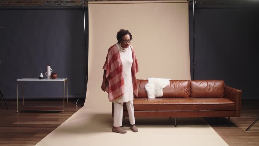 An elderly woman walking through a photography studio to sit on a sofa