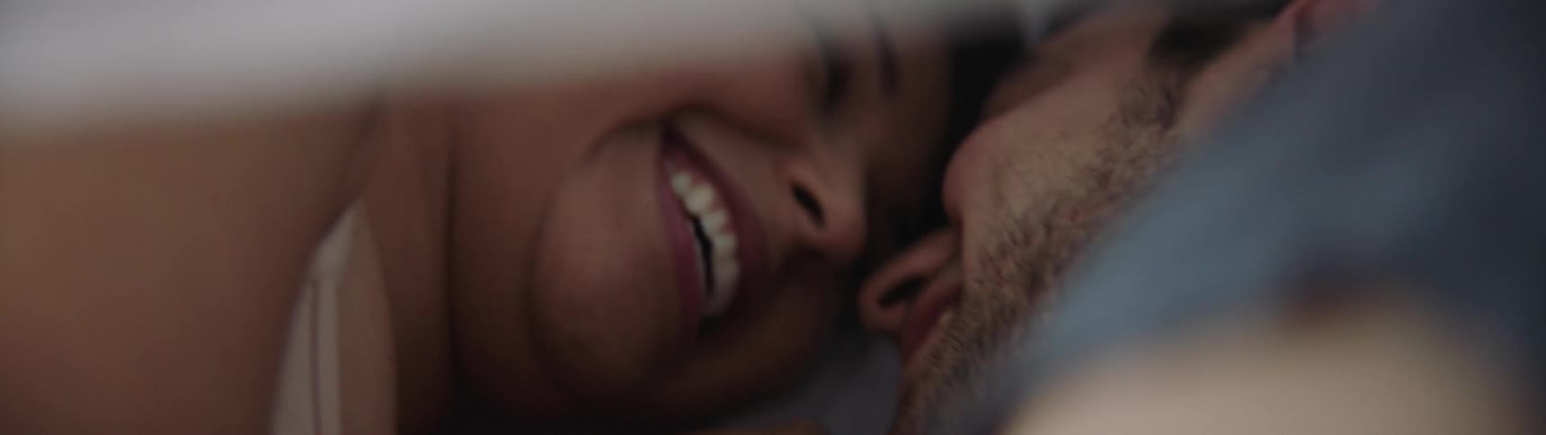 Couple laughing and snuggling under the covers in bed