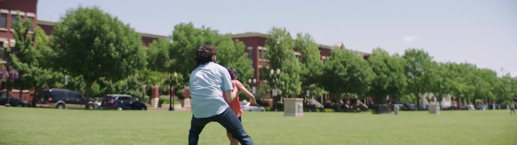 A dad chasing after a soccer ball with his son in the park picks him up and twirls him