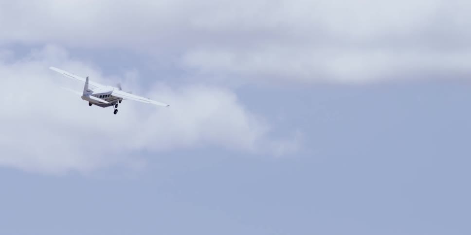 A small plane rising into a cloudy blue sky