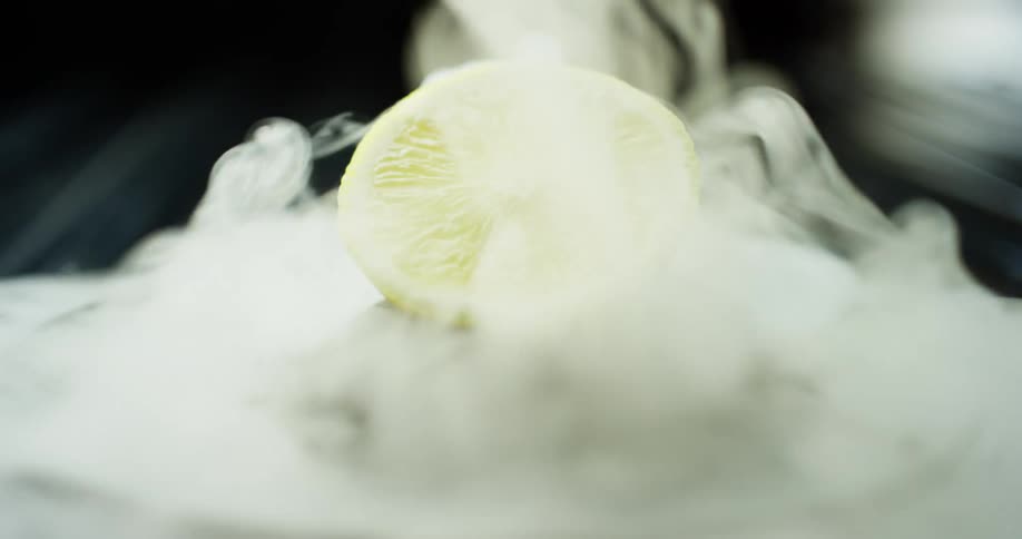 A glass lifts off of a lemon wedge covered in smoke