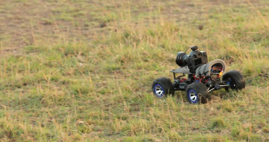A remote control car carries a camera across the ground in the daytime