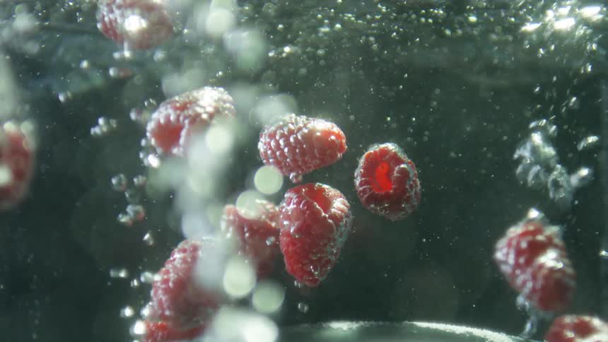 Red raspberries drop into a container of bubbling water