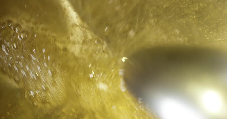 A metal spoon stirs a golden fluid in a metal pan
