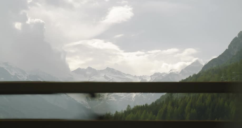 A forest and a mountain range seen from the window of a moving car