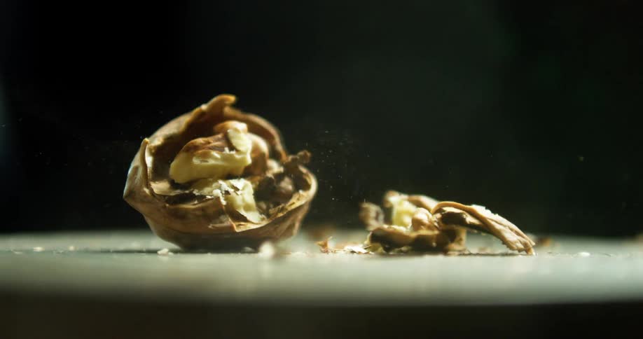 A walnut in front of a back drop is smashed by a hammer