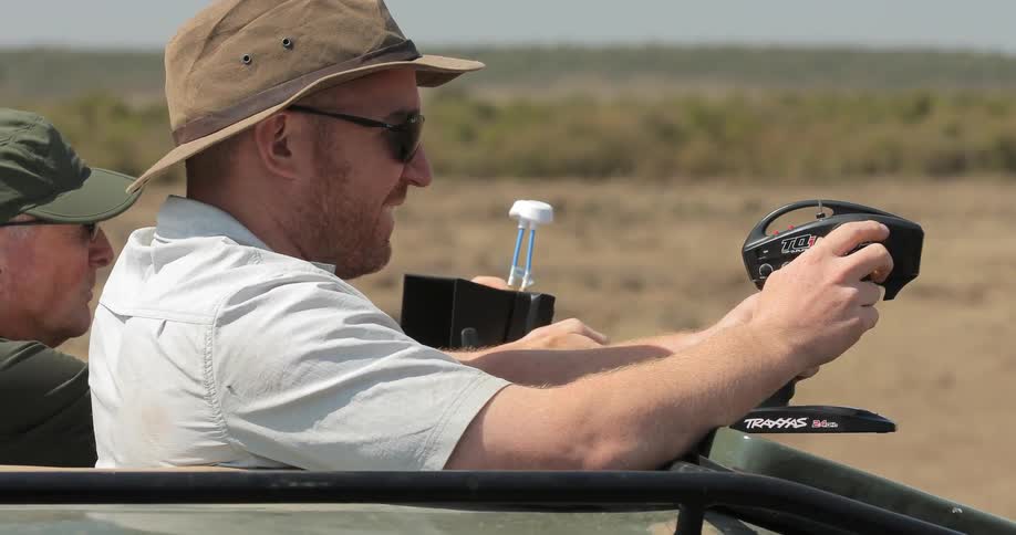 Two men stand through the top of a jeep observing something out of camera range
