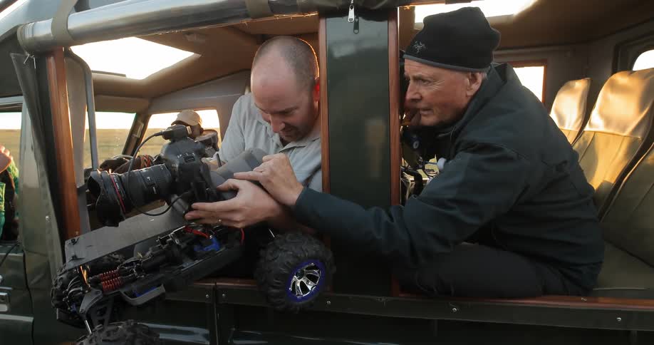 Two men sit in a jeep adjusting a camera on a motorized vehicle