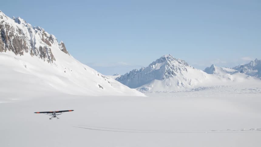 An airplane takes off from a snow covered field at the base of a mountain