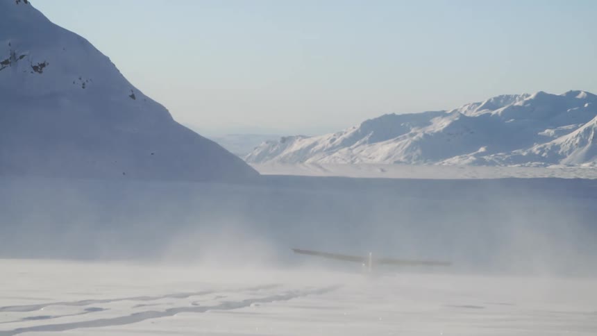 An airplane taking off in the snow with mountains in the background