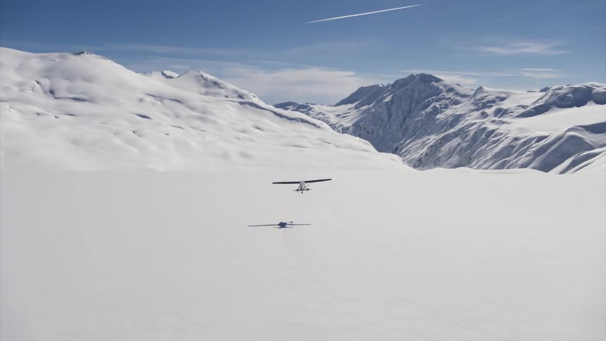 An airplane taking off in the snow with mountains and the sky in the background