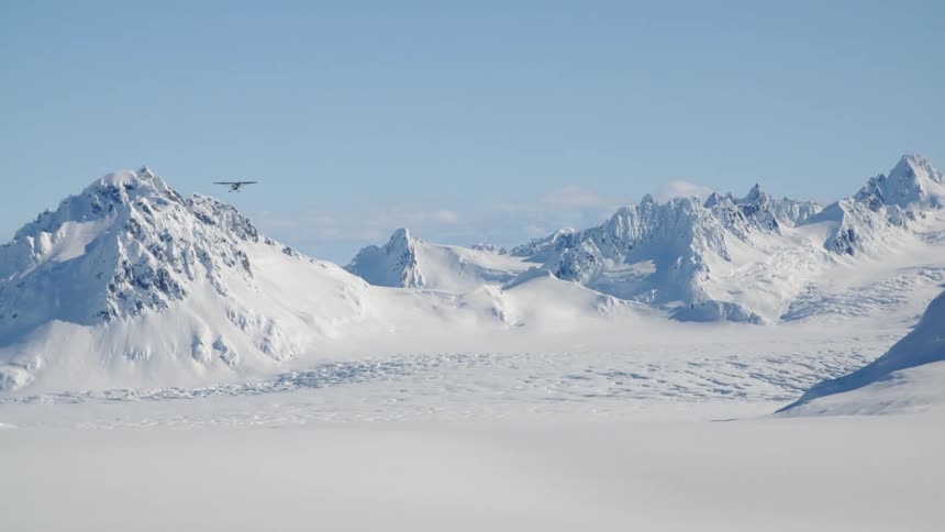 An airplane flies over a snow covered mountain range