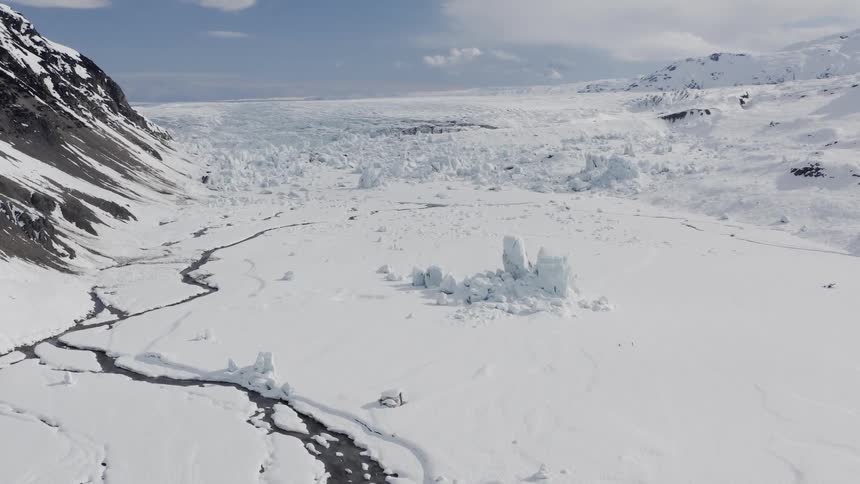 A cracked and snow covered frozen landscape at the base of a mountain in the arctic