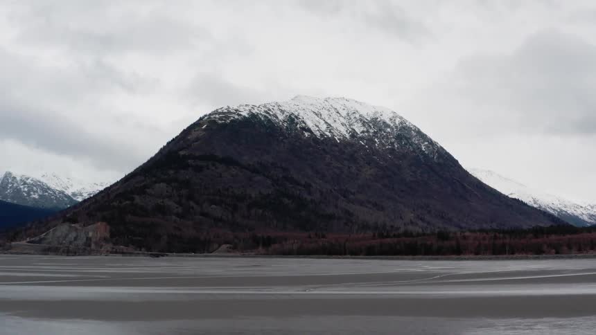 A mountain with snow on its peak sits next to a body of water