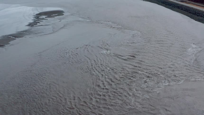 The water surface ripples and swirls with snow capped mountains on the horizon