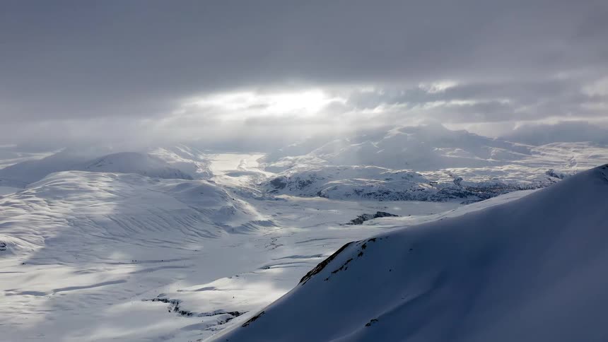 Aerial timelapse of sunlight filtering through clouds over a snow covered landscape