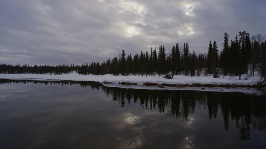 Clouds move over pine forest and lake in winter