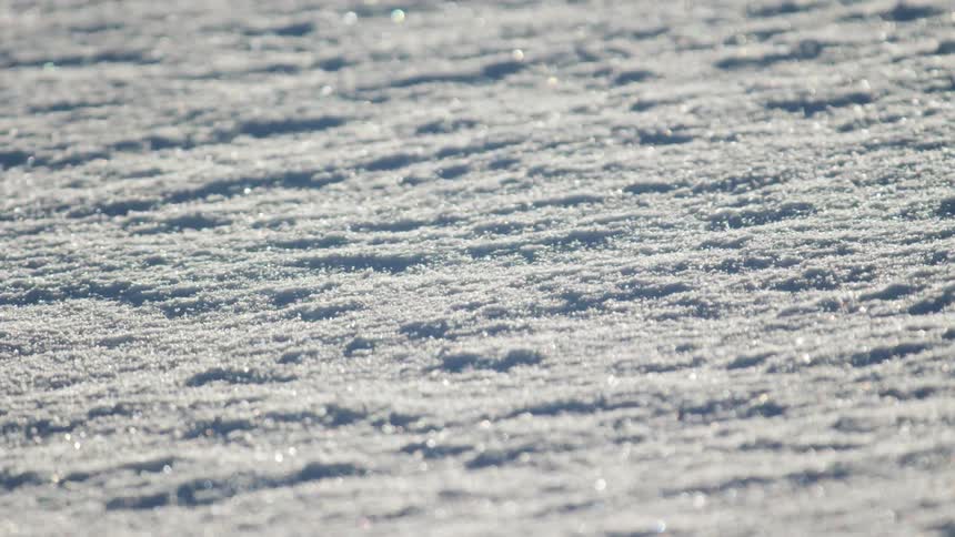 Snow is blown across ground dotted with glinting ice