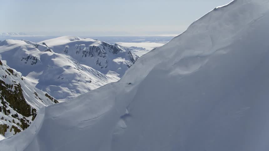 A mountain slope gives way to a snow choked valley