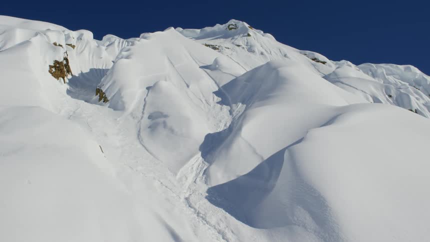 A snow covered mountain slope under a clear deep blue sky