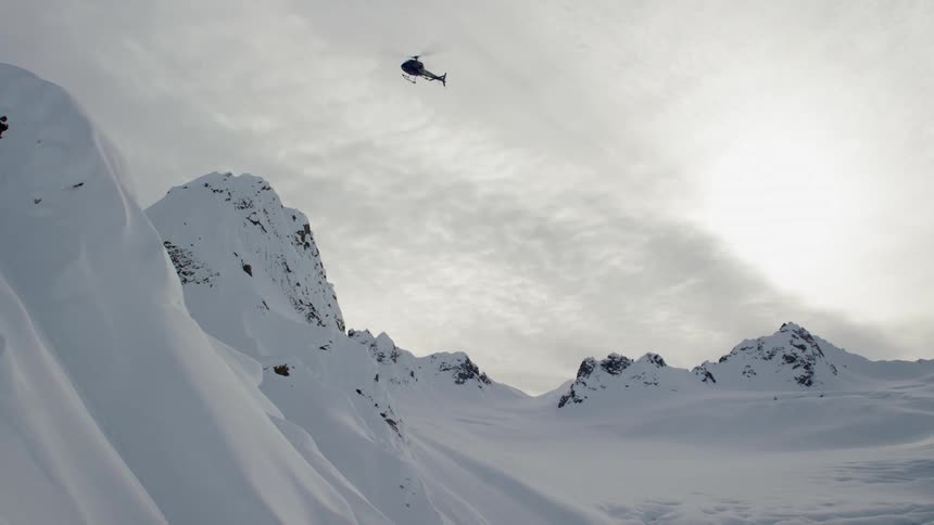A helicopter hovers over a snowy mountain range and valley