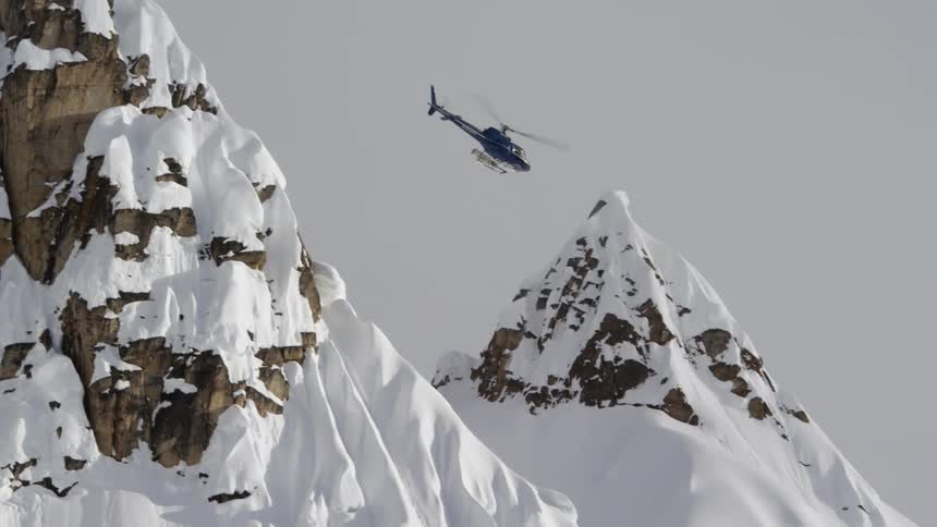 A helicopter flies close to snow covered mountain peaks