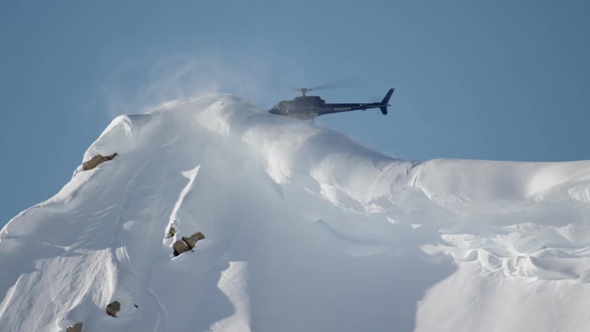 Helicopter lands on the snow covered peak of a mountain range