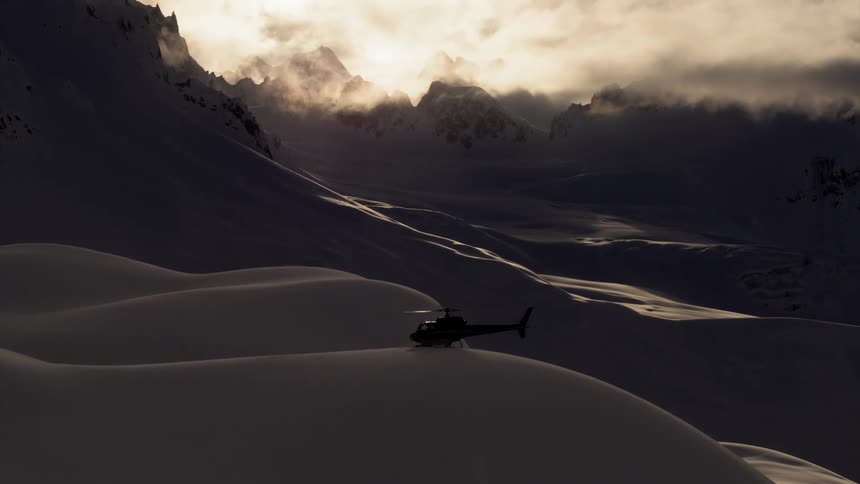 A helicopter attempts a landing on a deep snow drift on a mountain