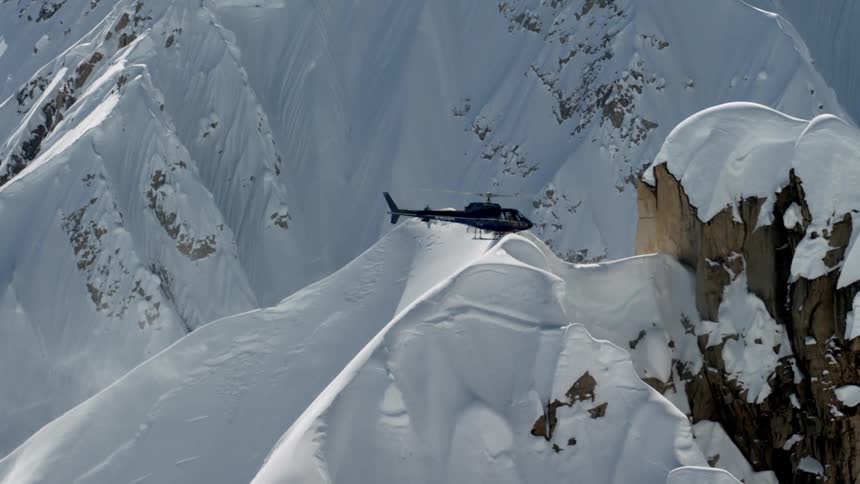 Dark colored helicopter hovers over snow covered mountain