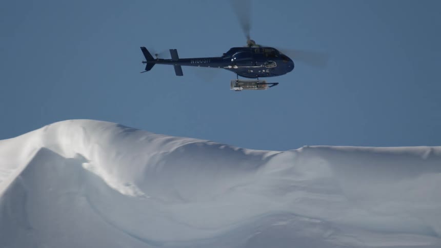 Helicopter circles over snow covered mountain ridge