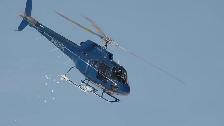 Slow motion shot of helicopter flying with its landing gear covered in snow